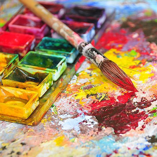 Ein bunter Aquarellkasten mit Pinsel der auf einer Unterlage mit Farbkleksen liegt