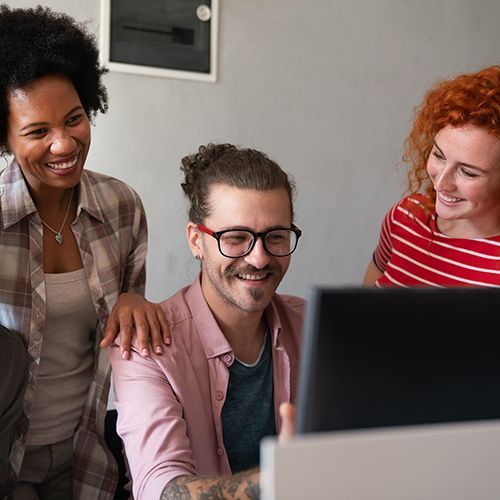 Eine Gruppe von jungen Menschen sitzen vor einem Bildschirm und schauen sich etwas lächelnd an.