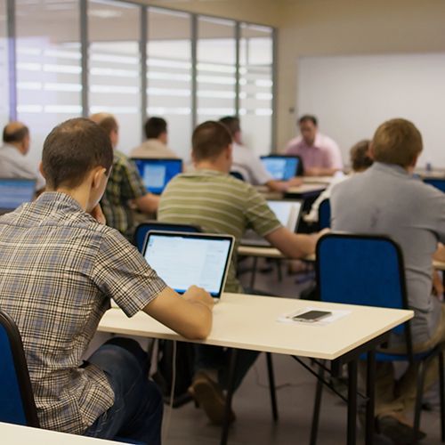 In einem Coputerraum sitzen Männer mit dem Rücken zur Kamera vor Laptops.