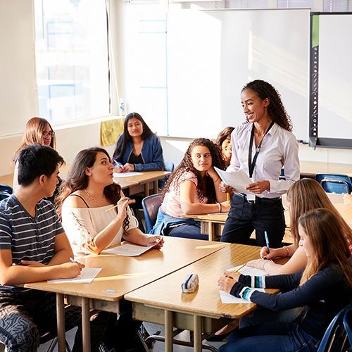 Eine weibliche Dozentin steht vor einem Tisch in einem Kursraum und erklärt den Kursteilnehmenden etwas